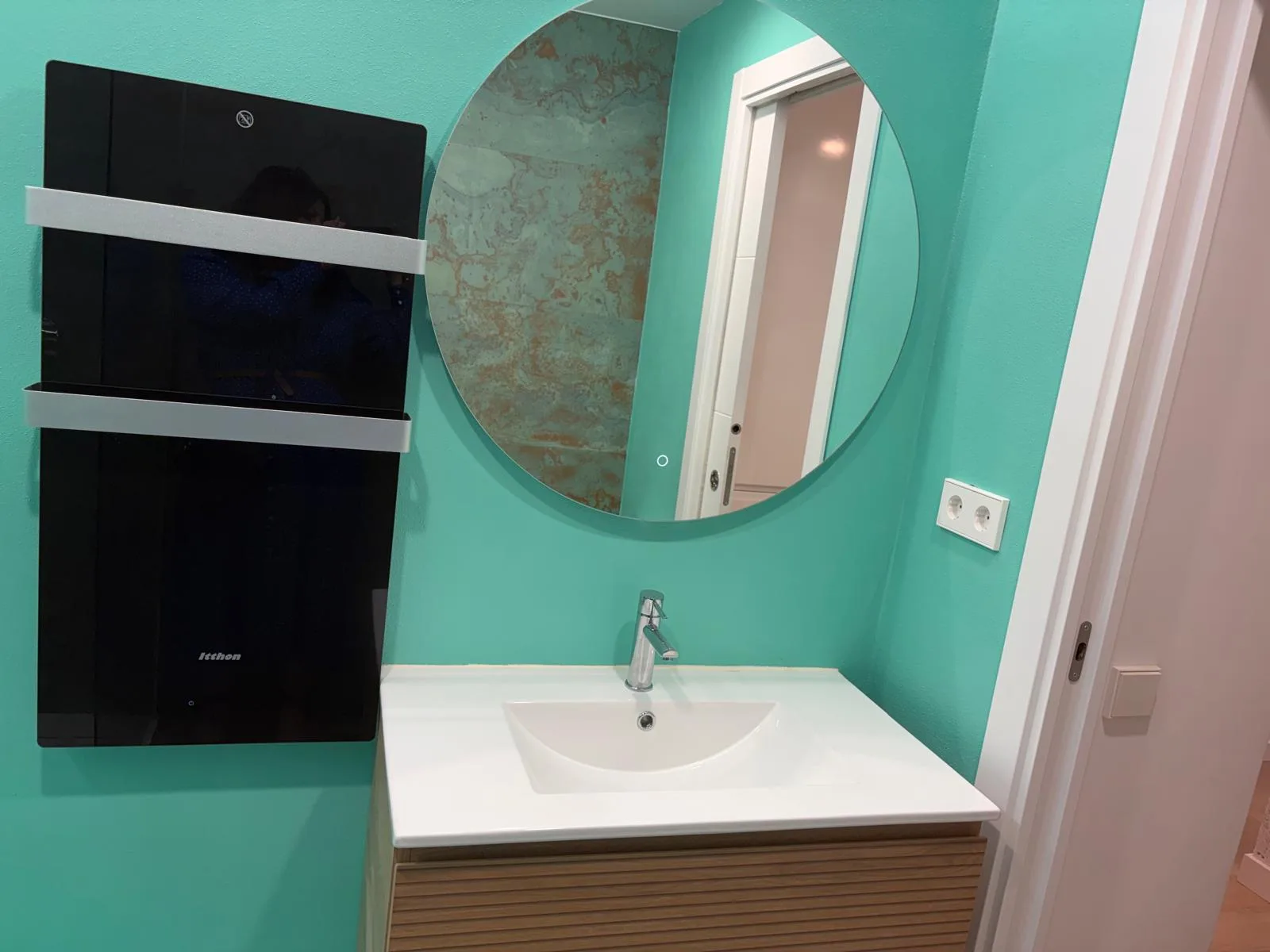 Baño con paredes turquesas, lavabo blanco, espejo circular y radiador negro