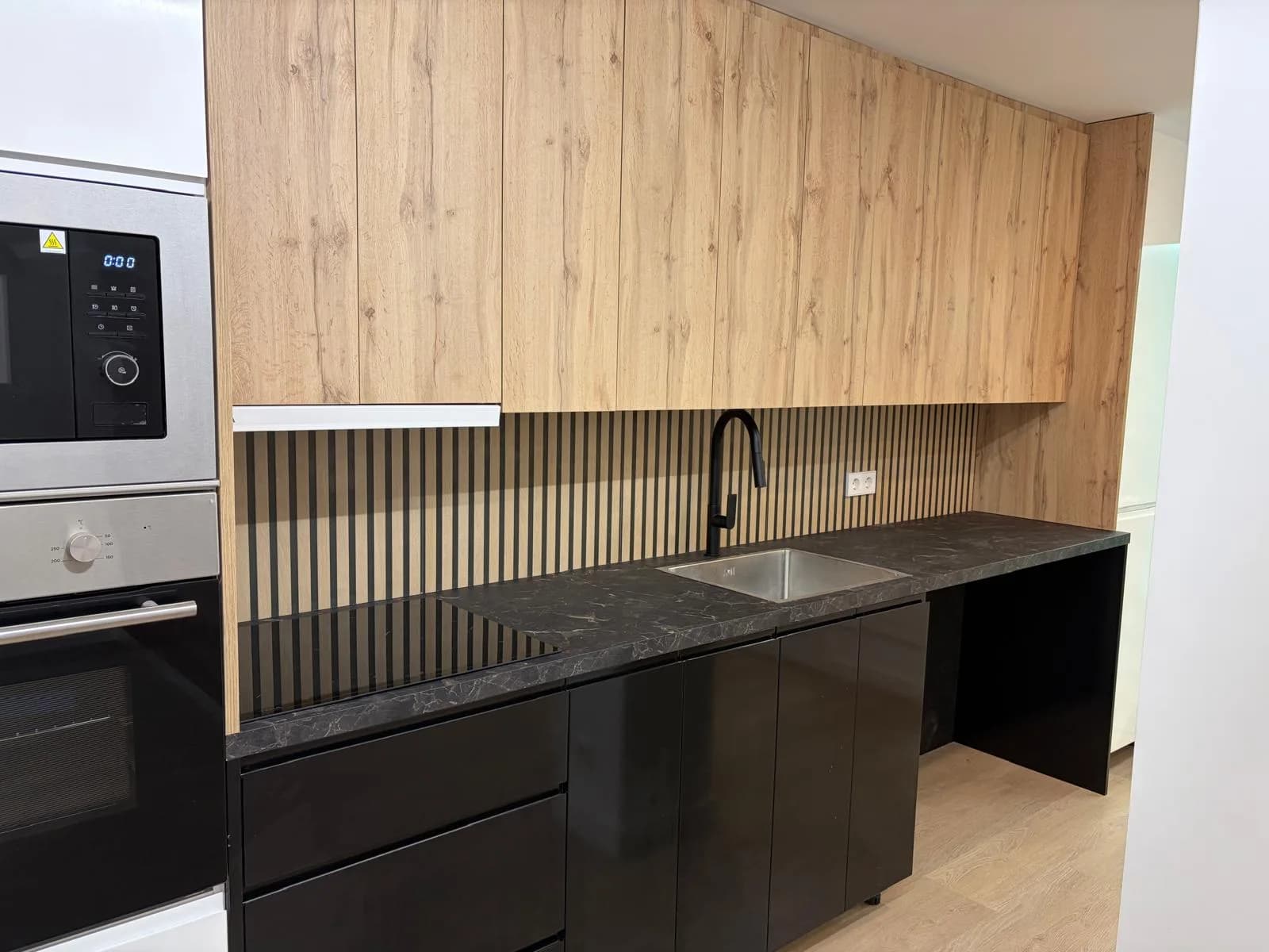 Cocina de una reforma interior con muebles de madera y negro, encimera oscura y fregadero